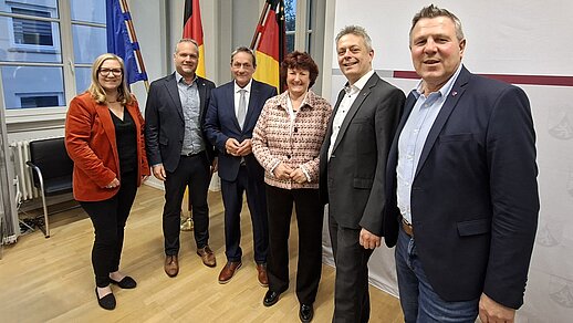 Gruppenbild vor drei Fahnen in einem Sitzungsraum
