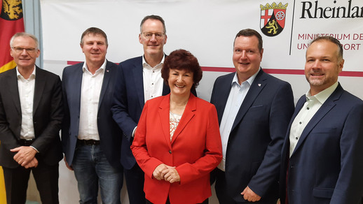  Gruppenbild mit sechs Personen vor einer Wand mit Logo von Rheinland-Pfalz